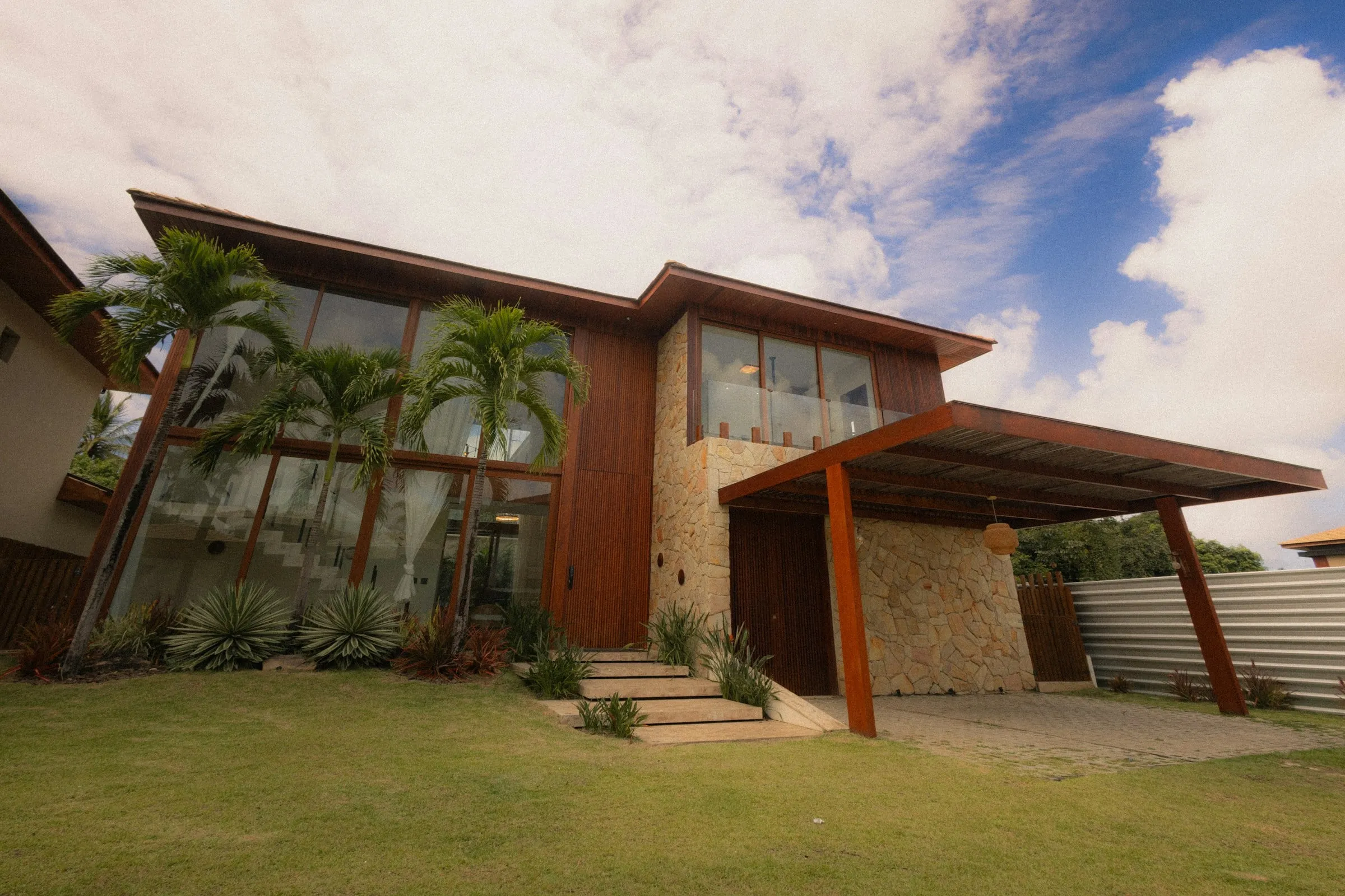 Casa de madeira e pedra com palmeiras e jardim frontal em Alto de Pinheiros