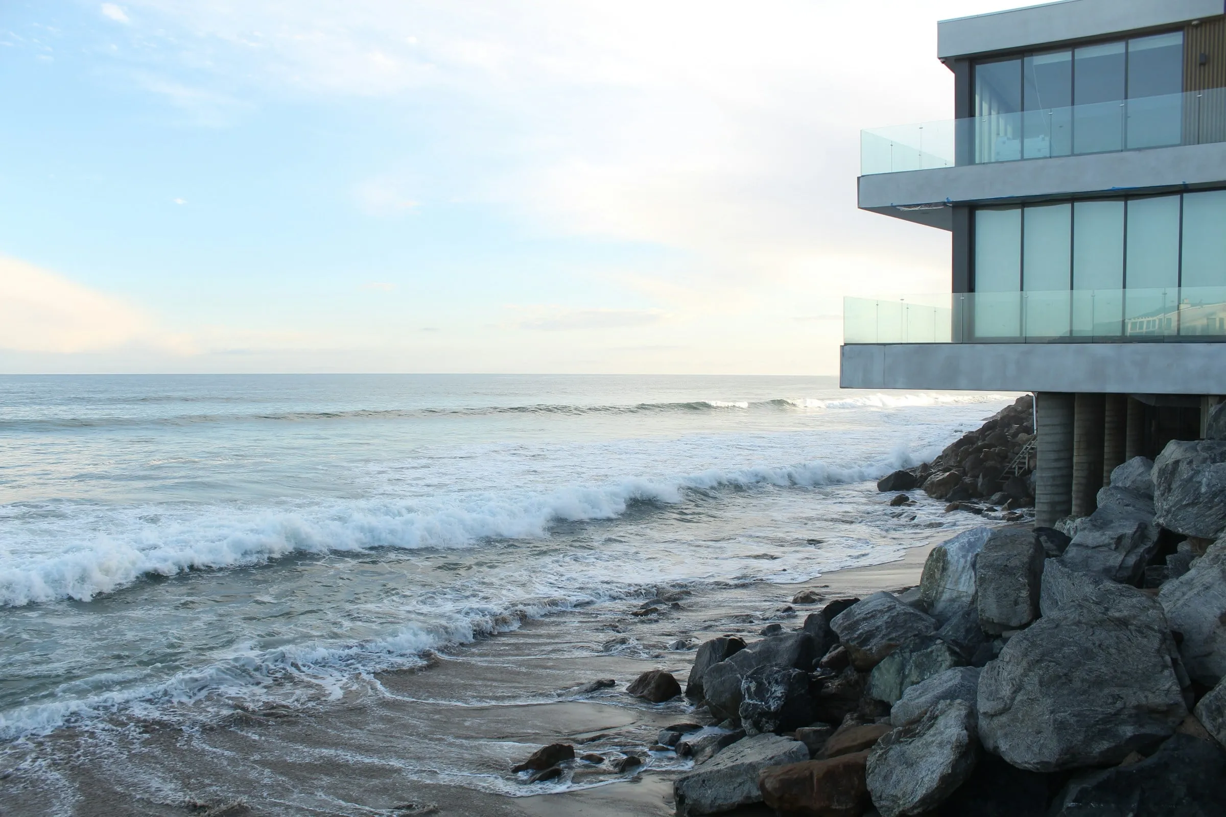 Casa contemporânea de vidro sobre as pedras, diante das ondas do mar